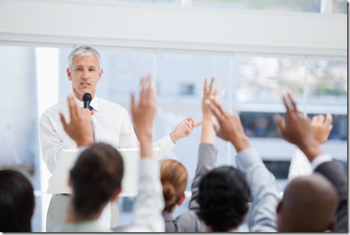 Businessman holding a microphone while looking at a business team with raised arms