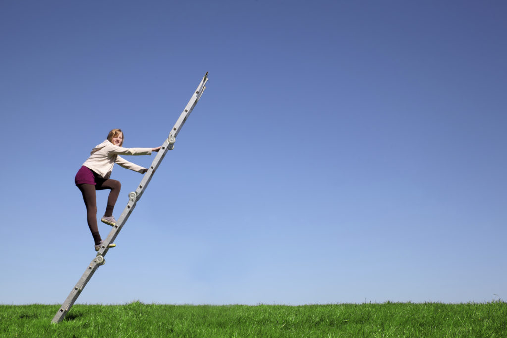 Young girl climbs a ladder on green meadow with blue sky
