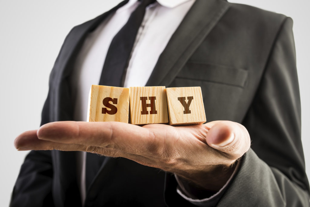 Businessman holding wooden alphabet blocks reading - Shy - balanced in the palm of his hand.