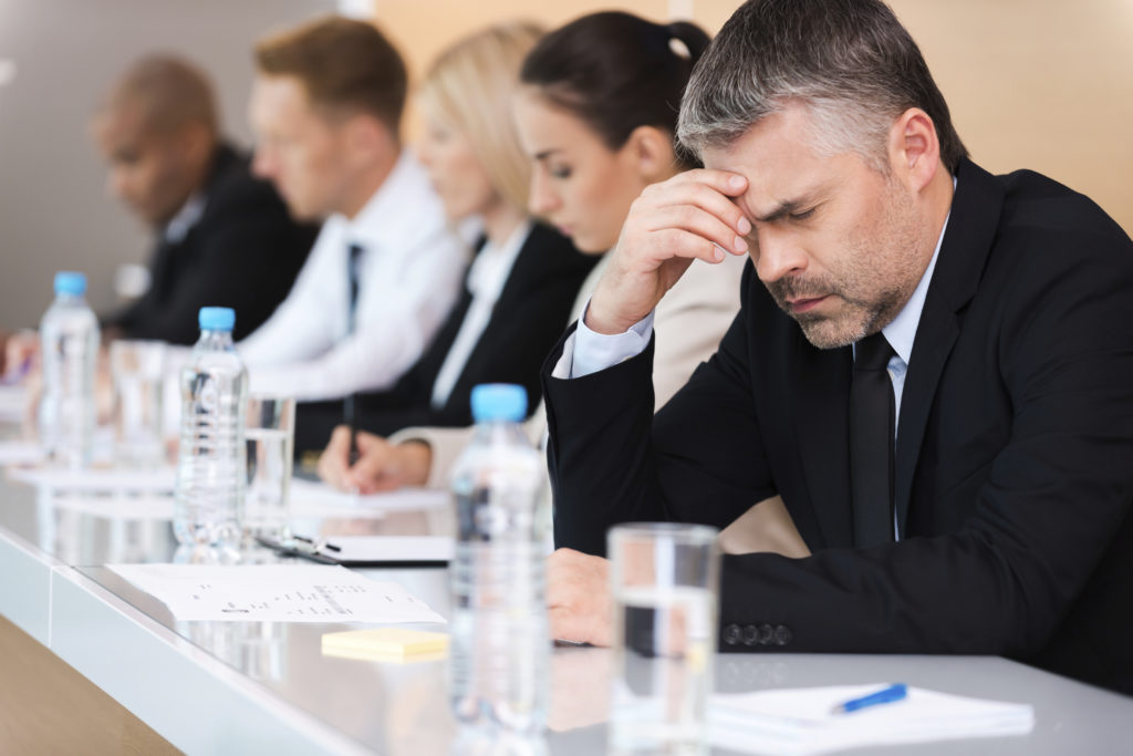 Suffering from headache. Side view of depressed mature businessman touching head with hand with people sitting in a row behind him