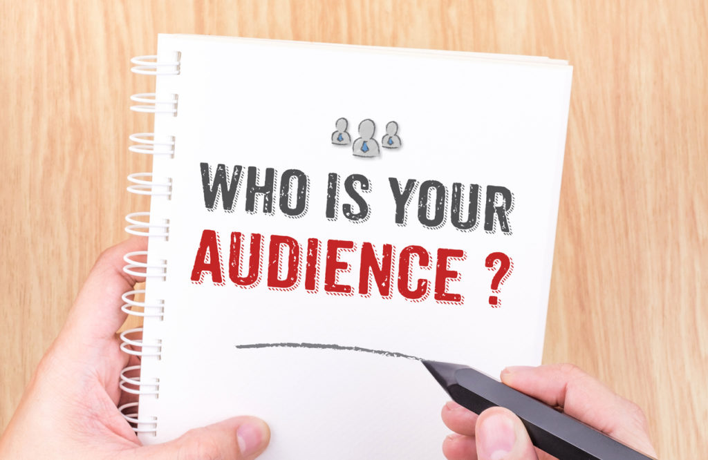 Who is your audience? word on white ring binder notebook with hand holding pencil on wood table,Business concept.