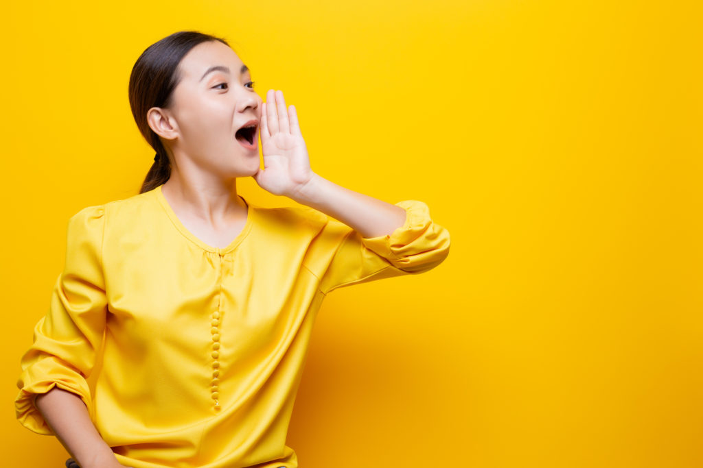 Woman in yellow dress talking in front of yellow background