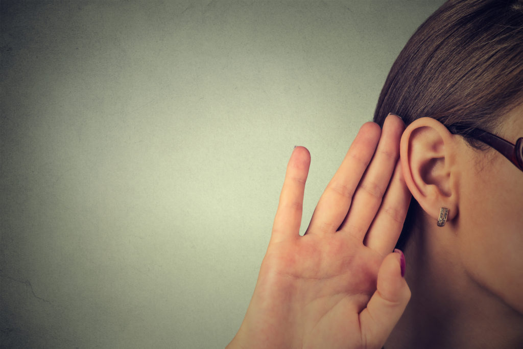 A woman listening with her hand at her ear