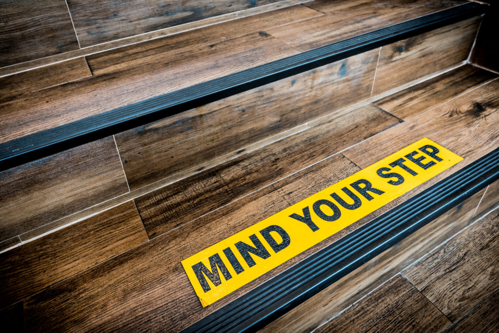 Mind your step sticker sign pasted on wooden stair.