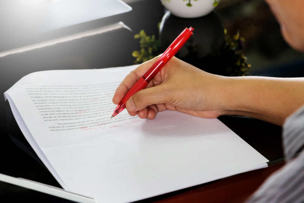 Hand holding red pen to correct proofreading paper