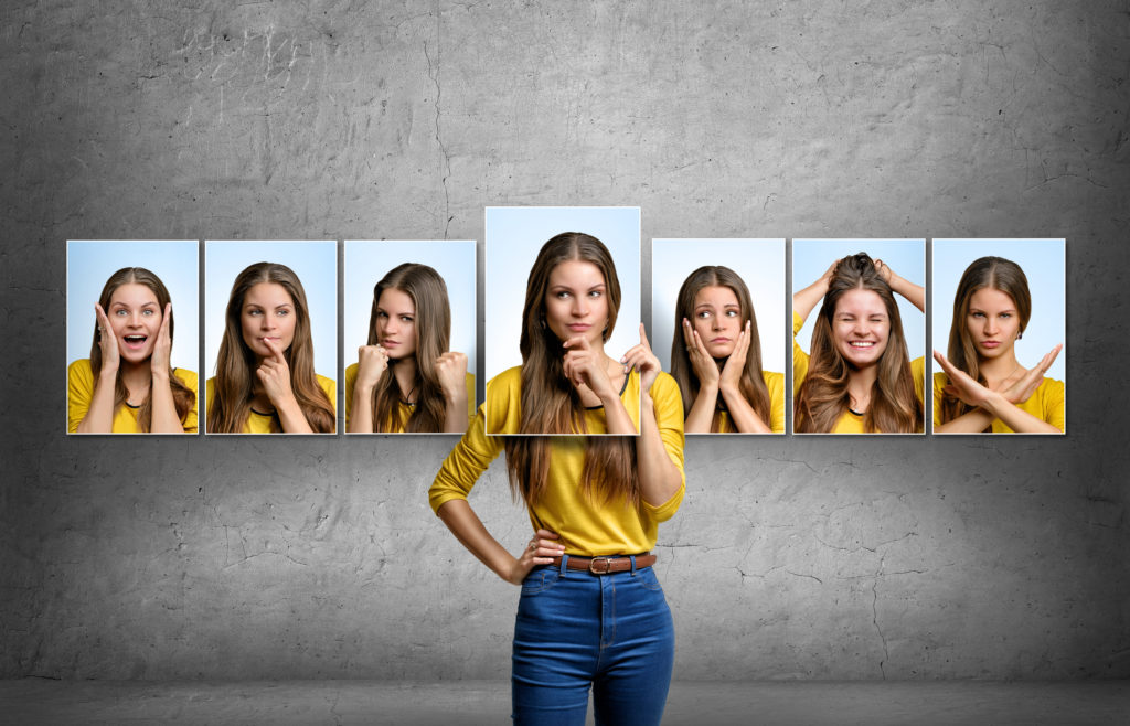 Young woman holds and changes face portraits with different emotions