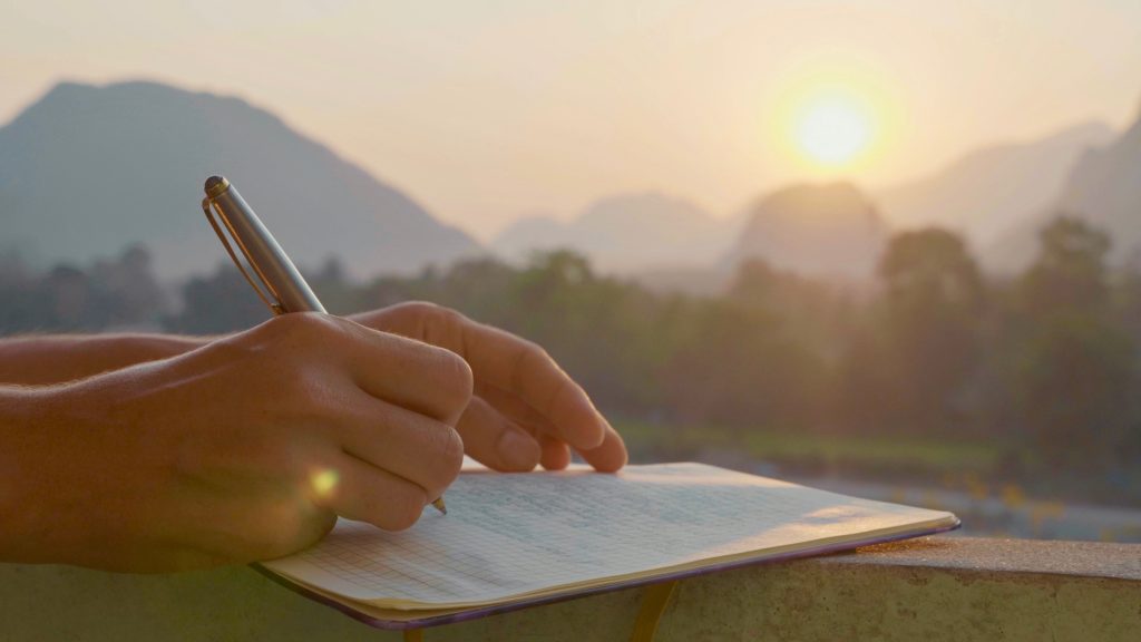 Young woman writing travel notes in diary during sunrise