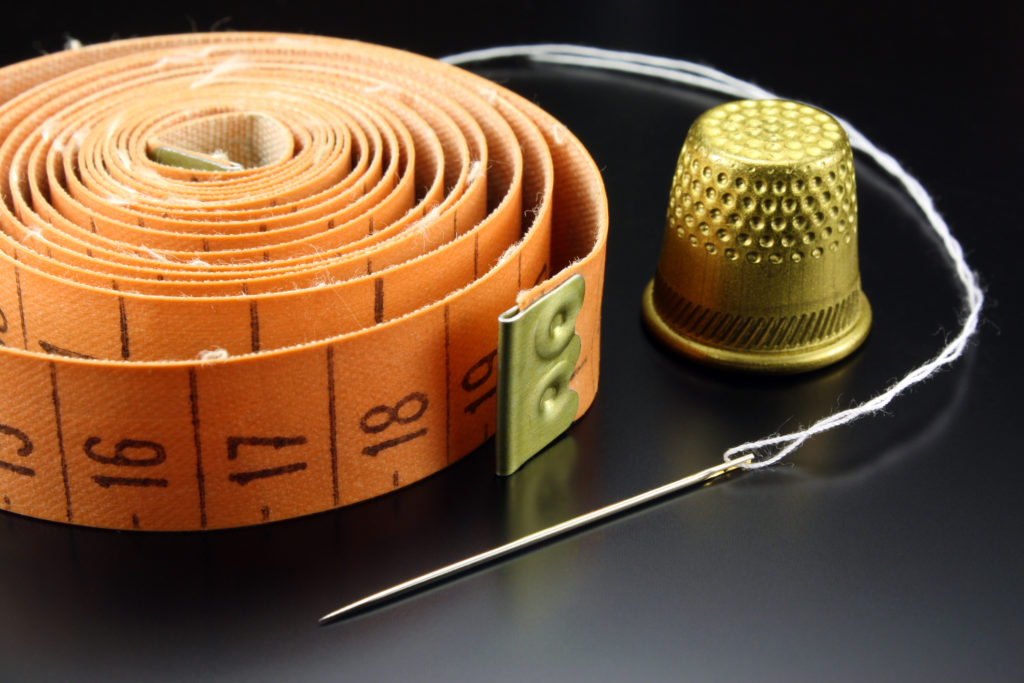 A thimble, tape measure, and needle with thread