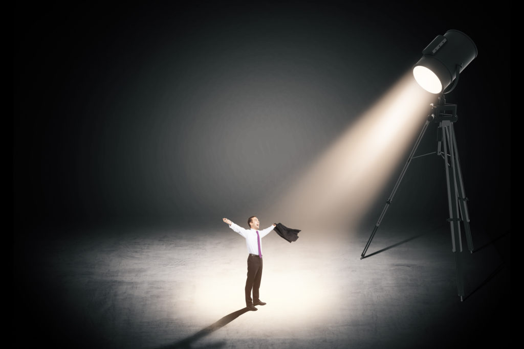 Business man standing under a spotlight with arms outstretched