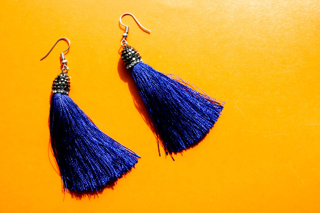 Deep blue tassel earrings on shiny orange background. Females accessories.