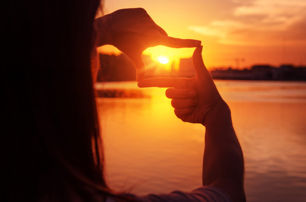 Woman hands making frame gesture with sunset.
