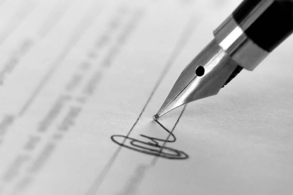 a pen writing a signature on contract